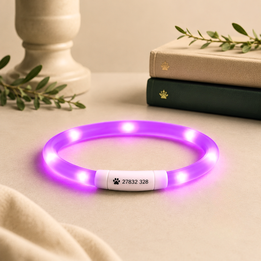 A glowing purple LED pet collar with a white customizable center section displaying a paw print and the numbers '27832 328', styled on a beige tabletop with books and a candle in the background.